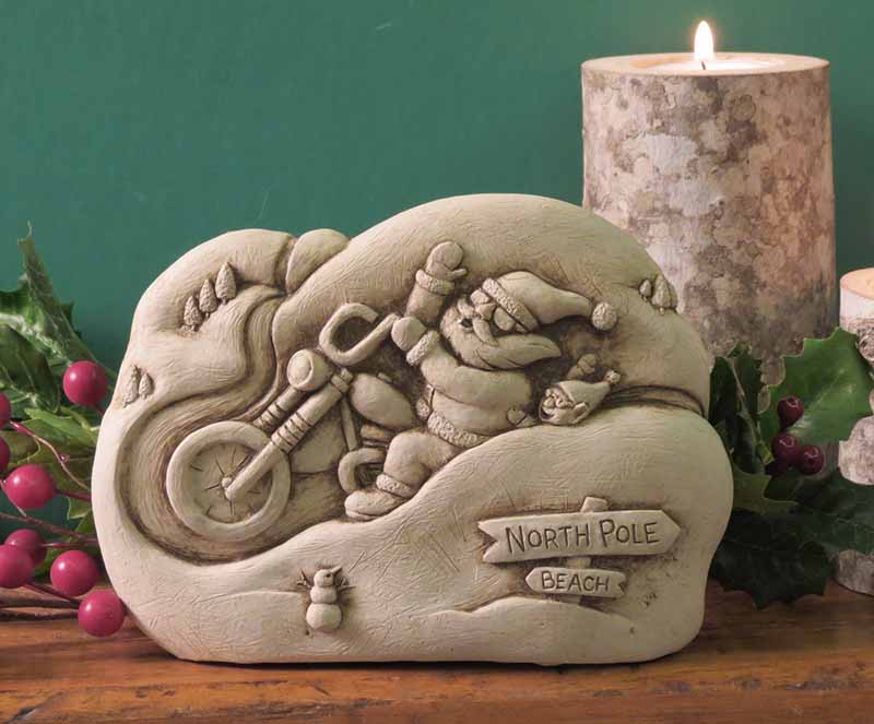 Santa motorcycle plaque on a wooden mantel with holly and a lit birch candle